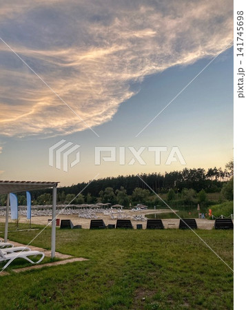 Beach area with sun loungers and umbrellas near a lake under a dramatic evening sky 141745698