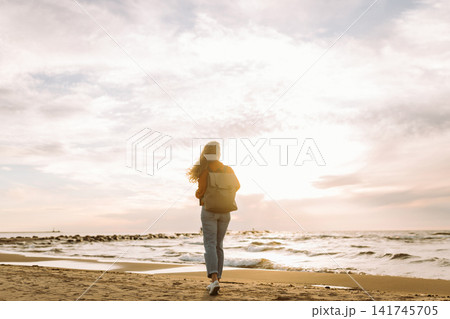 Beautiful woman on beach at sunset. Cold weather. Tourist, active lifestyle, relax concept. Beautiful woman on beach at sunset. Cold weather. Tourist, active lifestyle, relax concept. 141745705