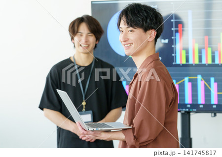 オフィスでディスプレイを前に会話する若い日本人男性2人 オフィスでディスプレイを前に会話する若い日本人男性2人 141745817