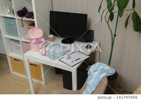Craft desk displaying an assortment of acrylic yarn, skeins of thread and knitting needles. Laptop and pattern book accessories. Table for crochet learning. DIY workspace. Crafts Hobbies workplace. Craft desk displaying an assortment of acrylic yarn, skeins of thread and knitting needles. Laptop and pattern book accessories. Table for crochet learning. DIY workspace. Crafts Hobbies workplace. 141745956