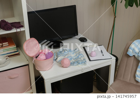 Craft desk displaying an assortment of acrylic yarn, skeins of thread and knitting needles. Laptop and pattern book accessories. Table for crochet learning. DIY workspace. Crafts Hobbies workplace. Craft desk displaying an assortment of acrylic yarn, skeins of thread and knitting needles. Laptop and pattern book accessories. Table for crochet learning. DIY workspace. Crafts Hobbies workplace. 141745957