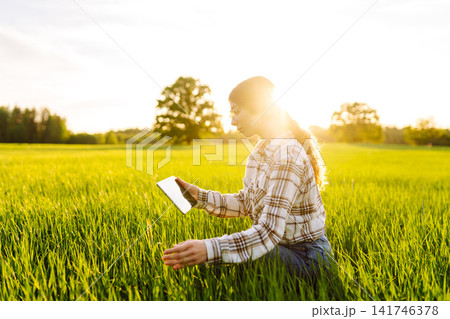 Young woman agronomist works on a modern digital tablet on a green wheat field. Young woman agronomist works on a modern digital tablet on a green wheat field. 141746378