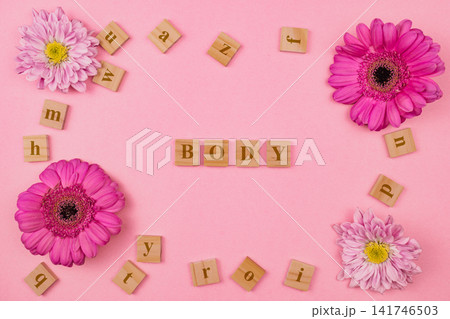 Top view of word BODY spelled with wooden letter tiles surrounded by pink flowers on bright background for body positivity, care and self-love concept design 141746503
