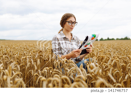 Farmer checking crop growth with clipboard in golden wheat field. Smart farming. Agribusiness. 141746757
