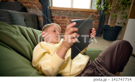 Five-year-old boy reclining with tablet during casual leisure time at home. Five-year-old boy reclining with tablet during casual leisure time at home. 141747754