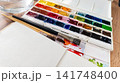 Watercolor Painting Set with Open Palette Brushes and Empty Sketchbook on Wooden Desk 141748400