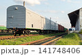 Grey Freight Train Railway Cars Standing on Tracks Near Industrial Warehouse Platform 141748406
