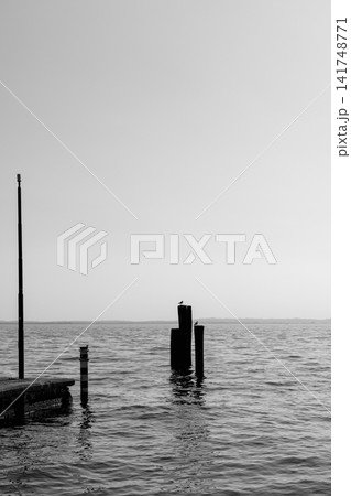 Black and white mooring posts and small pier on calm Lake Garda water in Italy 141748771