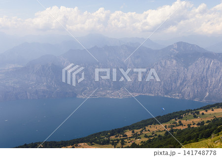 Lake Garda mountain view from Monte Baldo with a small paraglider in the sky Lake Garda mountain view from Monte Baldo with a small paraglider in the sky 141748778