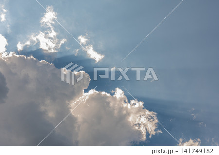Sun rays breaking through dramatic white clouds in bright blue sky 141749182