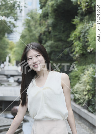 緑豊かな公園で微笑むノースリーブの若い女性 緑豊かな公園で微笑むノースリーブの若い女性 141749514