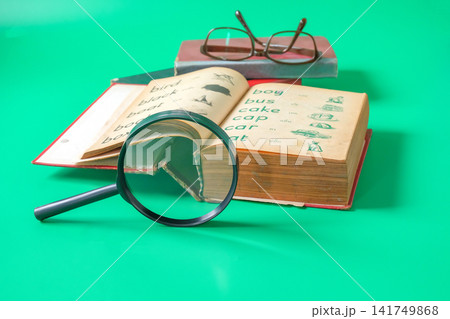 A magnifying glass and Old English book , textbook for learning language. A magnifying glass and Old English book , textbook for learning language. 141749868