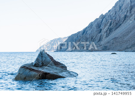 Coastal view of Dahab, Egypt, featuring the Red Sea and Sinai mountains. Rocky shoreline with clear water and distant mountains. Coastal view of Dahab, Egypt, featuring the Red Sea and Sinai mountains. Rocky shoreline with clear water and distant mountains. 141749955