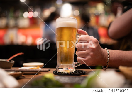 居酒屋で冷えた生ビールを持つ男性の手元 居酒屋で冷えた生ビールを持つ男性の手元 141750302