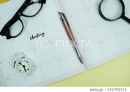 Meeting message written on calendar date with alarm clock, glasses and magnifying glass on yellow background 141750315