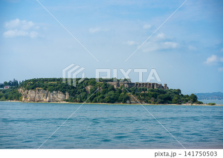 Rocky island surrounded by the waters of Lake Garda, Italy. Concept of travel, nature, geology, exploration and peaceful recreation Rocky island surrounded by the waters of Lake Garda, Italy. Concept of travel, nature, geology, exploration and peaceful recreation 141750503