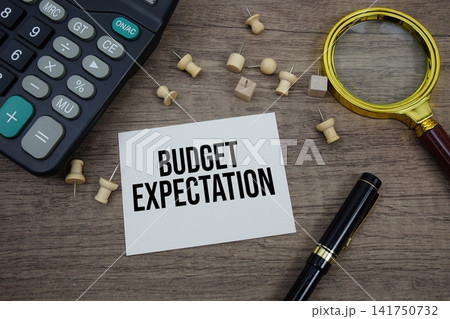 Budget Expectation text written on notepad with pen, alarm clock, magnifying glass and calculator on wooden background Budget Expectation text written on notepad with pen, alarm clock, magnifying glass and calculator on wooden background 141750732