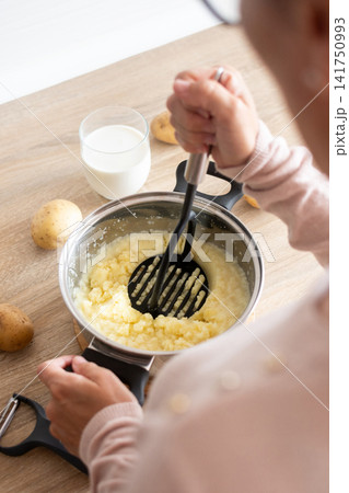 Person mashing boiled potatoes in a saucepan Person mashing boiled potatoes in a saucepan 141750993