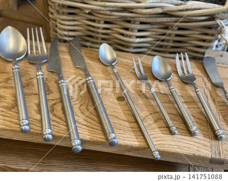 Cutlery set with various utensils on wooden board in front of woven basket, ideal for kitchen decor Cutlery set with various utensils on wooden board in front of woven basket, ideal for kitchen decor 141751088