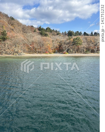 青森県十和田市の湖、十和田湖の11月に、遊覧船から見た陸地の小山の綺麗な紅葉と青空の風景です。 青森県十和田市の湖、十和田湖の11月に、遊覧船から見た陸地の小山の綺麗な紅葉と青空の風景です。 141751232