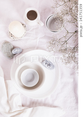 Coarse linen drapery for a kitchen table with ceramic dishes in white tones top and vertical view 141751359