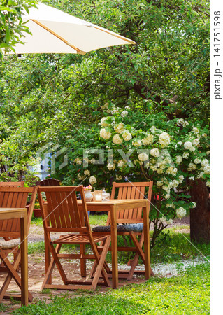 Cozy garden patio with wooden furniture and flowering shrubs in summer. Outdoor cafe, restaurant 141751598