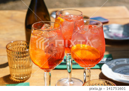 Three glasses or refreshing orange spritz cocktails with ice and citrus slices on sunny summer patio Three glasses or refreshing orange spritz cocktails with ice and citrus slices on sunny summer patio 141751601