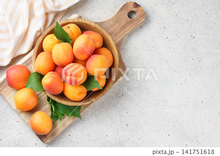 Fresh ripe apricots fruits in wooden bowl on cutting board over light stone background, copy space 141751618