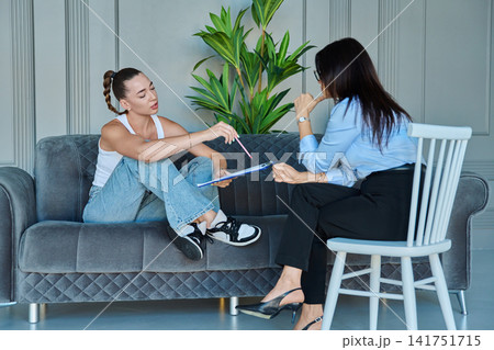 Young woman holding clipboard and talking to female psychologist Young woman holding clipboard and talking to female psychologist 141751715
