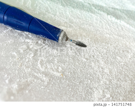 Close-up of a blue electric nail drill with carbide cutter bit covered in white acrylic dust on a table. Ideal for nail salon, manicure service, hardware pedicure, beauty industry, and nail care  141751748