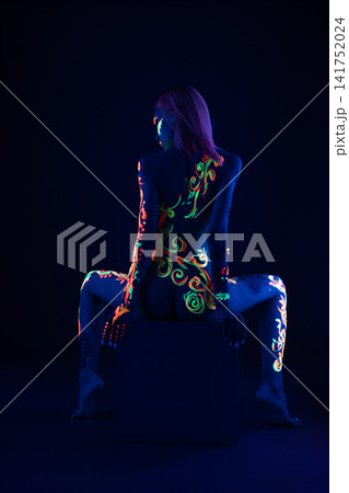 Woman with glowing neon body paint in dark studio Woman with glowing neon body paint in dark studio 141752024