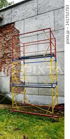 Scaffolding stands against a brick wall at a construction site in daytime Scaffolding stands against a brick wall at a construction site in daytime 141752783
