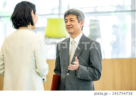 オフィスで会話をするスーツ姿のシニア男女 オフィスで会話をするスーツ姿のシニア男女 141754738