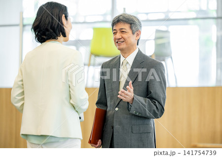オフィスで会話をするスーツ姿のシニア男女 オフィスで会話をするスーツ姿のシニア男女 141754739