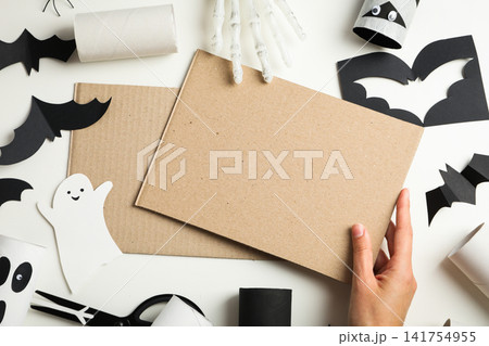 Halloween. Hand reaching for blank cardboard amidst colorful halloween crafts Halloween. Hand reaching for blank cardboard amidst colorful halloween crafts 141754955