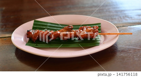 Grilled meat skewer plate banana leaf on wooden table with savory glaze Grilled meat skewer plate banana leaf on wooden table with savory glaze 141756118