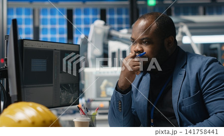 African american master engineer reviews operations in a solar tech plant, ensuring factory activity to meet green energy targets. Specialist uses tablet for manufacturing efficiency. Camera B. 141758441