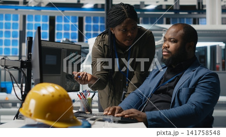 African american team of specialists reviewing solar panel production systems during inspection, ensuring engineering accuracy and quality control. High tech industrial factory. Camera B. African american team of specialists reviewing solar panel production systems during inspection, ensuring engineering accuracy and quality control. High tech industrial factory. Camera B. 141758548