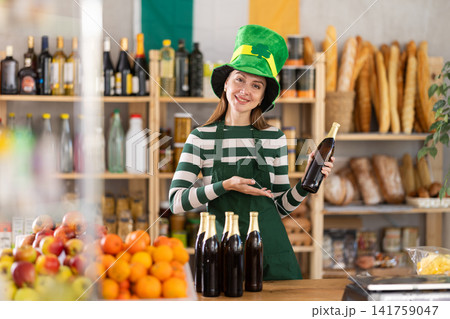 Positive friendly girl seller in traditional green Irish cap offers to buy Irish ale for St. Patrick Day celebration 141759047