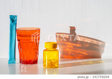 Glass of water with medicine bottle and supplement sachet on white table. Health and wellness concept Glass of water with medicine bottle and supplement sachet on white table. Health and wellness concept 141759204