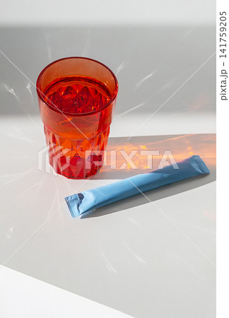 Red glass of water with light reflections and blue sachet on white surface. Red glass of water with light reflections and blue sachet on white surface. 141759205