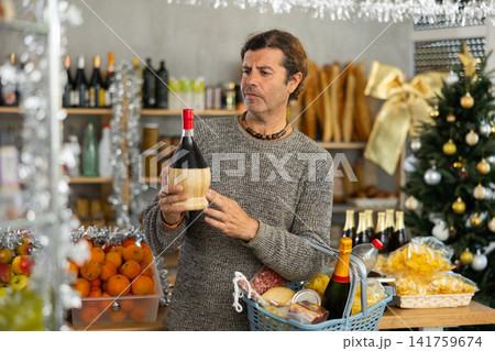 Thoughtful shopper selecting alcoholic drinks for Christmas festivities in grocery store Thoughtful shopper selecting alcoholic drinks for Christmas festivities in grocery store 141759674
