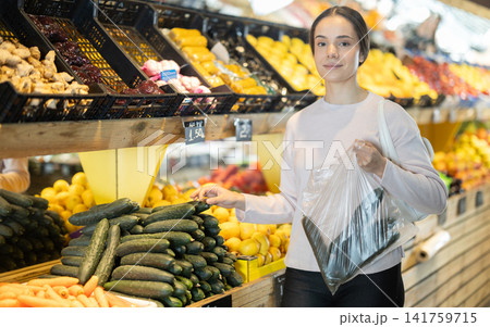 Young woman chooses cucumbers in store Young woman chooses cucumbers in store 141759715