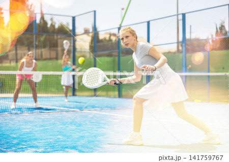 Woman actively playing paddle tennis on a court in a park against the background of glare 141759767
