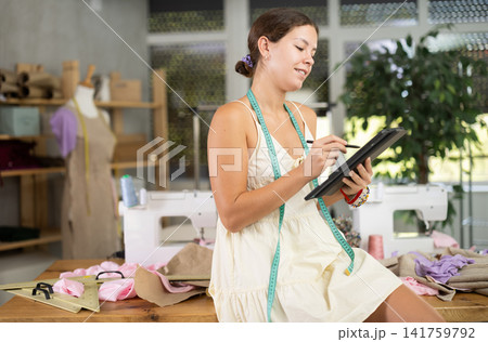 Young female dressmaker drawing on tablet in sewing workshop Young female dressmaker drawing on tablet in sewing workshop 141759792