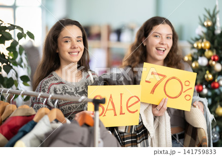Two girls with poster in hands announces X mas discounts Two girls with poster in hands announces X mas discounts 141759833