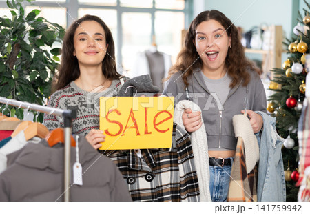Two young women presents sale sign in store Two young women presents sale sign in store 141759942