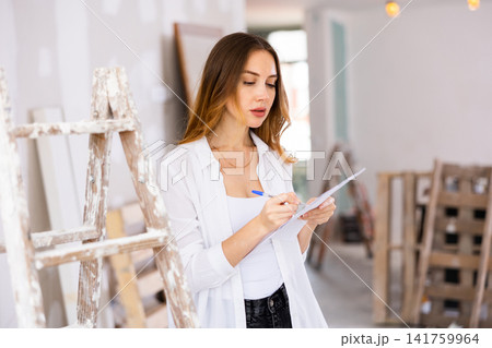 Woman designer checking documents during repair works Woman designer checking documents during repair works 141759964