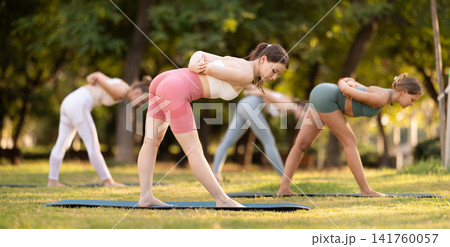 Athletic girls meditates in yoga pose parshvottanasana in summer sunny park. Demonstration of various yoga poses 141760057