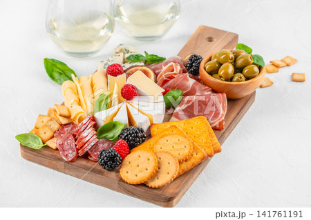 Elegant charcuterie board with cheeses, prosciutto, olives and wine on light background 141761191
